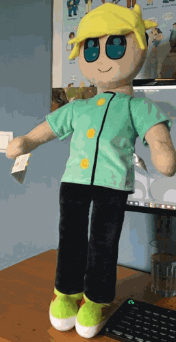 a stuffed doll wearing a green shirt and black pants is holding a piece of paper