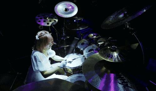 a woman in a white dress is playing the drums