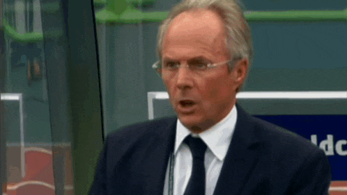a man wearing glasses and a suit stands in front of a microphone