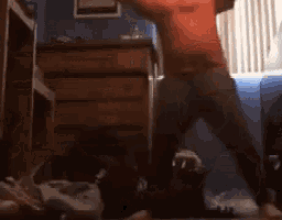 a man in a red shirt is dancing in front of a window in a room .