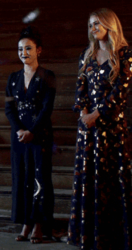 two women in long dresses are standing next to each other in front of a building .