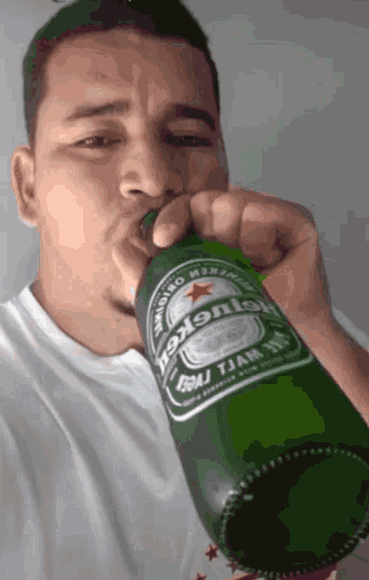 a man is drinking from a green bottle of heineken