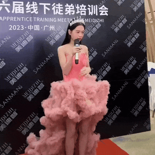 a woman in a pink dress is holding a microphone in front of a wall that says sanman