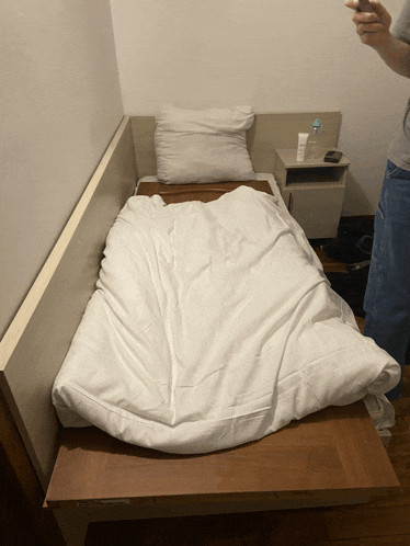 a person is standing next to a bed with a white blanket on it