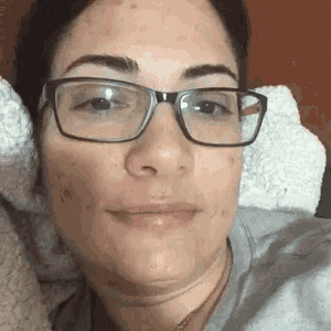 a woman wearing glasses is laying in bed with a pillow .