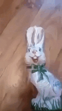a white easter bunny with a green bow on its neck is sitting on a wooden table .