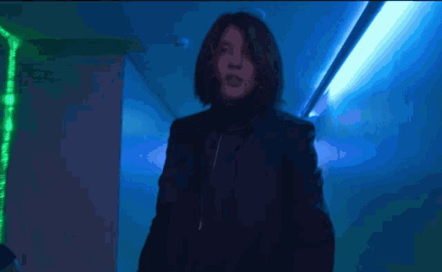 a woman in a black suit is walking down a dark hallway