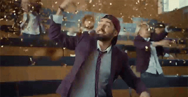 a man in a suit and tie is dancing in a classroom with confetti falling from the ceiling .