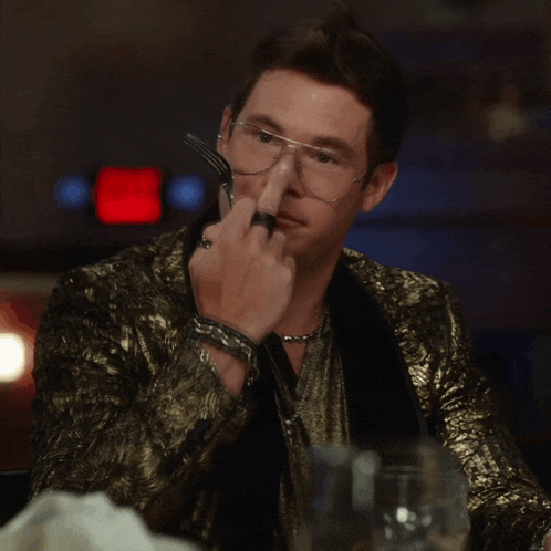 a man in a gold jacket and glasses holds a fork and knife