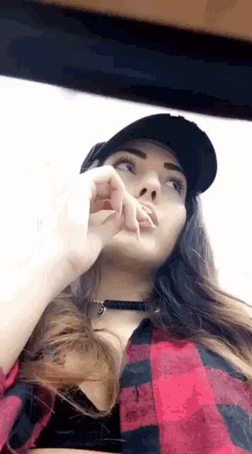 a woman wearing a plaid shirt and a baseball cap is looking up at the sky .