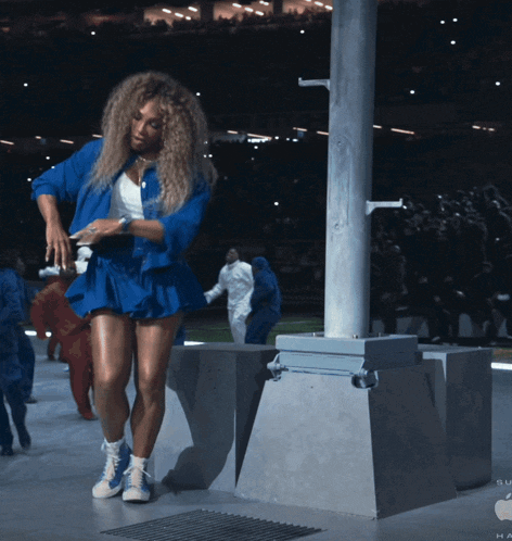 a woman in a blue jacket and shorts is standing next to a pole