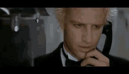 a man in a tuxedo and tie is talking on a phone .