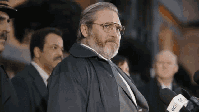a man with glasses and a beard stands in front of microphones that say cc