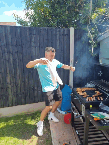 a man in a blue shirt is standing in front of a grill with smoke coming out of it