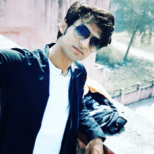 a young man wearing sunglasses and a white shirt stands on a balcony
