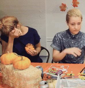 a couple of people sitting at a table with pumpkins and candy