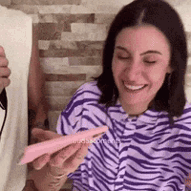 a woman in a zebra print shirt is smiling while holding a pink phone