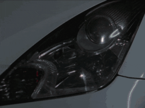 a close up of a car headlight with a reflection of a person 's face