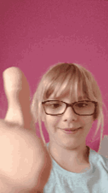 a young girl wearing glasses giving a thumbs up