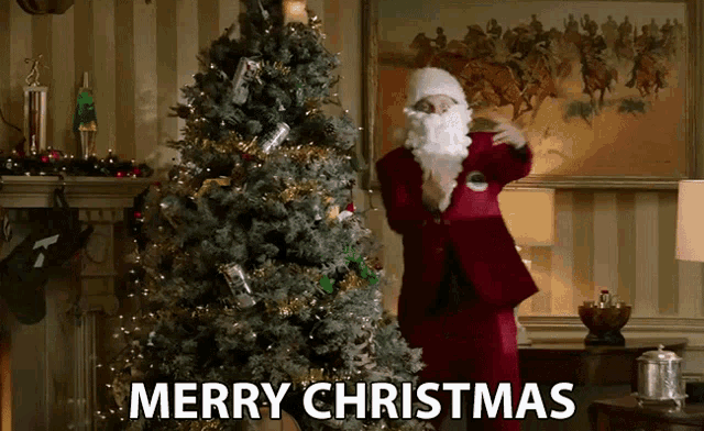 a man dressed as santa claus is standing in front of a christmas tree with the words merry christmas below him