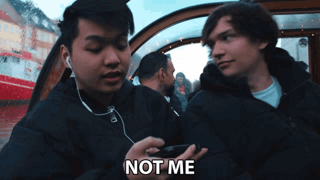 a man with ear buds looks at another man 's phone and says not me