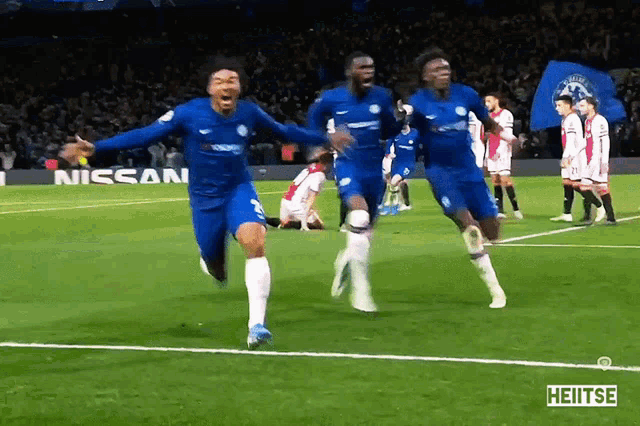 a group of soccer players are celebrating a goal on a field that has nissan written on it