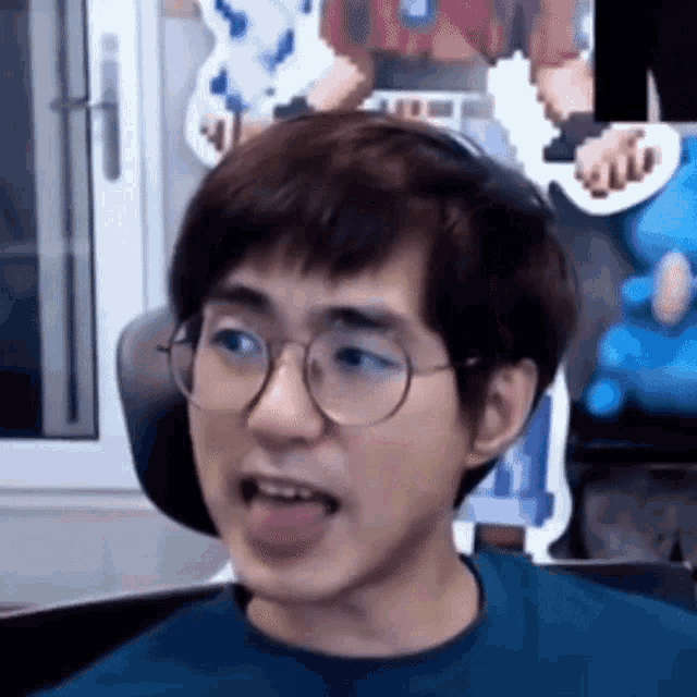 a man wearing glasses is sticking his tongue out while sitting in front of a computer .