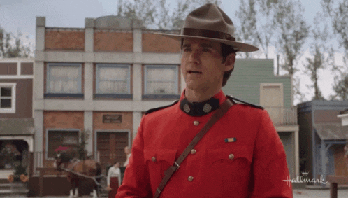 a man in a red uniform and hat is standing in front of a hallmark building