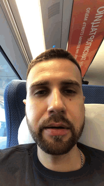 a man with a beard is sitting on a train with a sign above him that says " origami "