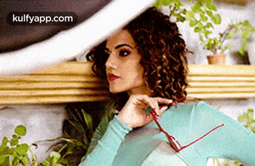 a woman with curly hair is holding a pair of glasses in her hand .
