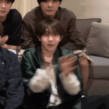 a group of young men are sitting on a couch and one of them has a green jacket on