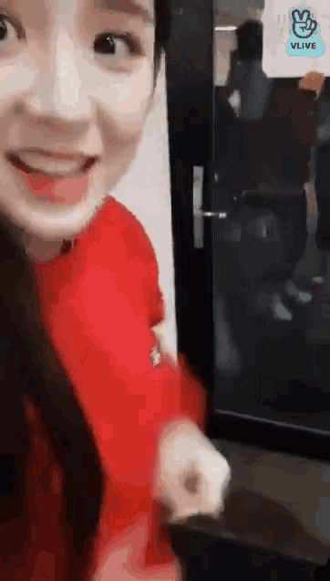a woman in a red sweater is standing in front of a door with a sign that says vlive on it .