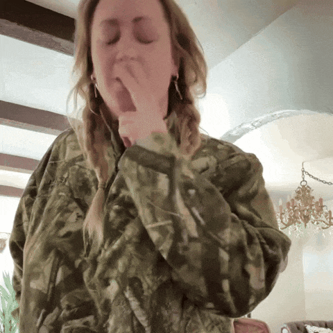 a woman wearing a camo jacket covering her mouth