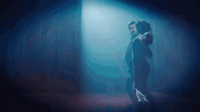 a man and a woman are dancing in a dark room under a blue light .