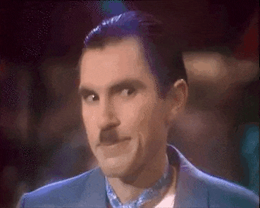 a man with purple hair and a mustache is wearing a blue suit and a blue tie .