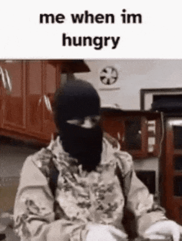 a man in a mask is sitting in a kitchen with the words `` me when im hungry '' written on the bottom .