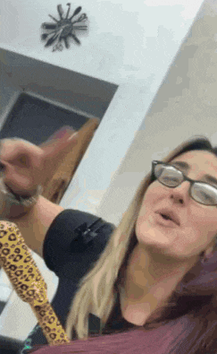 a woman wearing glasses is holding a lizard in her hand and making a funny face .