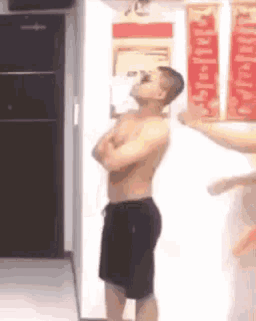 a shirtless man is standing in a hallway with his arms crossed and drinking from a bottle .