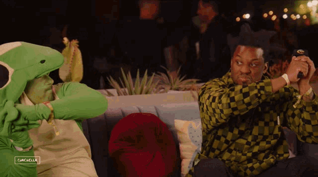 a man in a lizard costume sits next to a man in a checkered shirt with the word coachella on the bottom