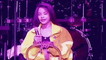 a woman in a yellow jacket is sitting on a drum set holding a tambourine .