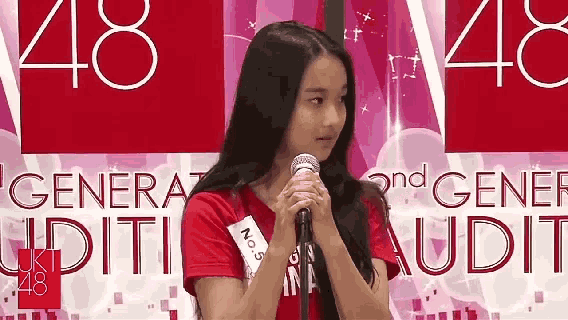 a girl in a red shirt is standing in front of a microphone