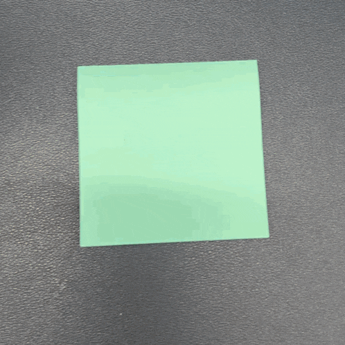 a green square piece of paper is laying on a black surface