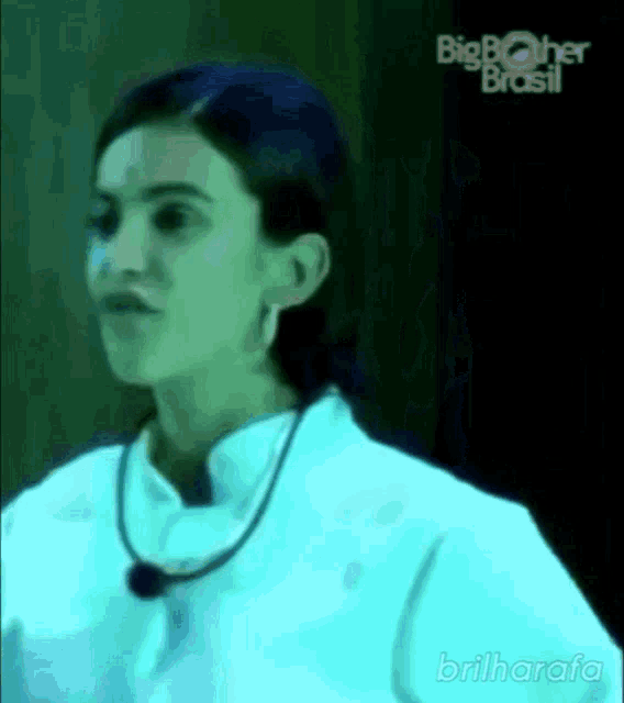 a woman in a white shirt with a necklace around her neck is standing in front of a big brother brasil logo .