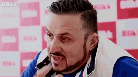 a man with a beard is talking on a cell phone in front of a pink and white background .