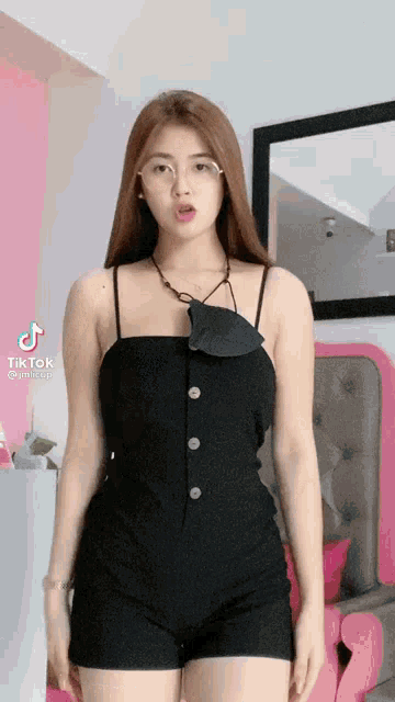 a woman in a black dress and shorts is standing in front of a pink chair and a mirror .