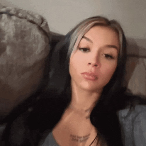 a woman with long black hair is sitting on a couch taking a selfie .