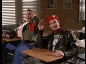 two men are sitting at desks in a classroom giving each other high fives