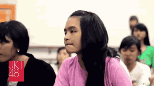 a girl in a pink shirt is sitting in front of a sign that says jkt48