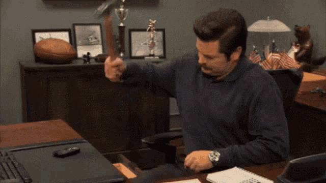 a man is sitting at a desk in an office holding a hammer .