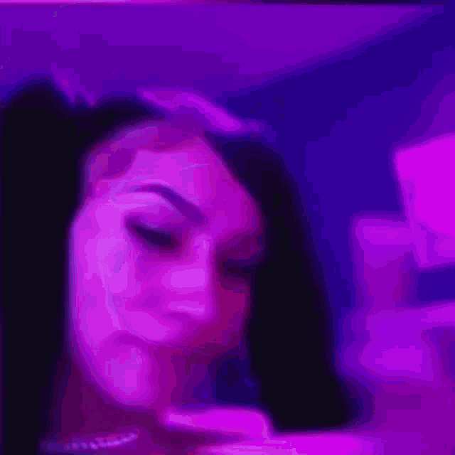 a close up of a woman 's face in front of a purple light .